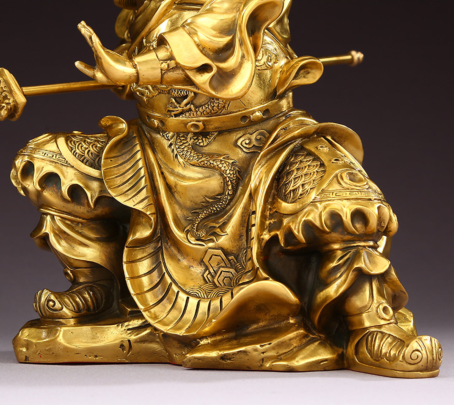 Close-up of lower body of brass Guan Yu statue featuring hollow design base and warrior stance.